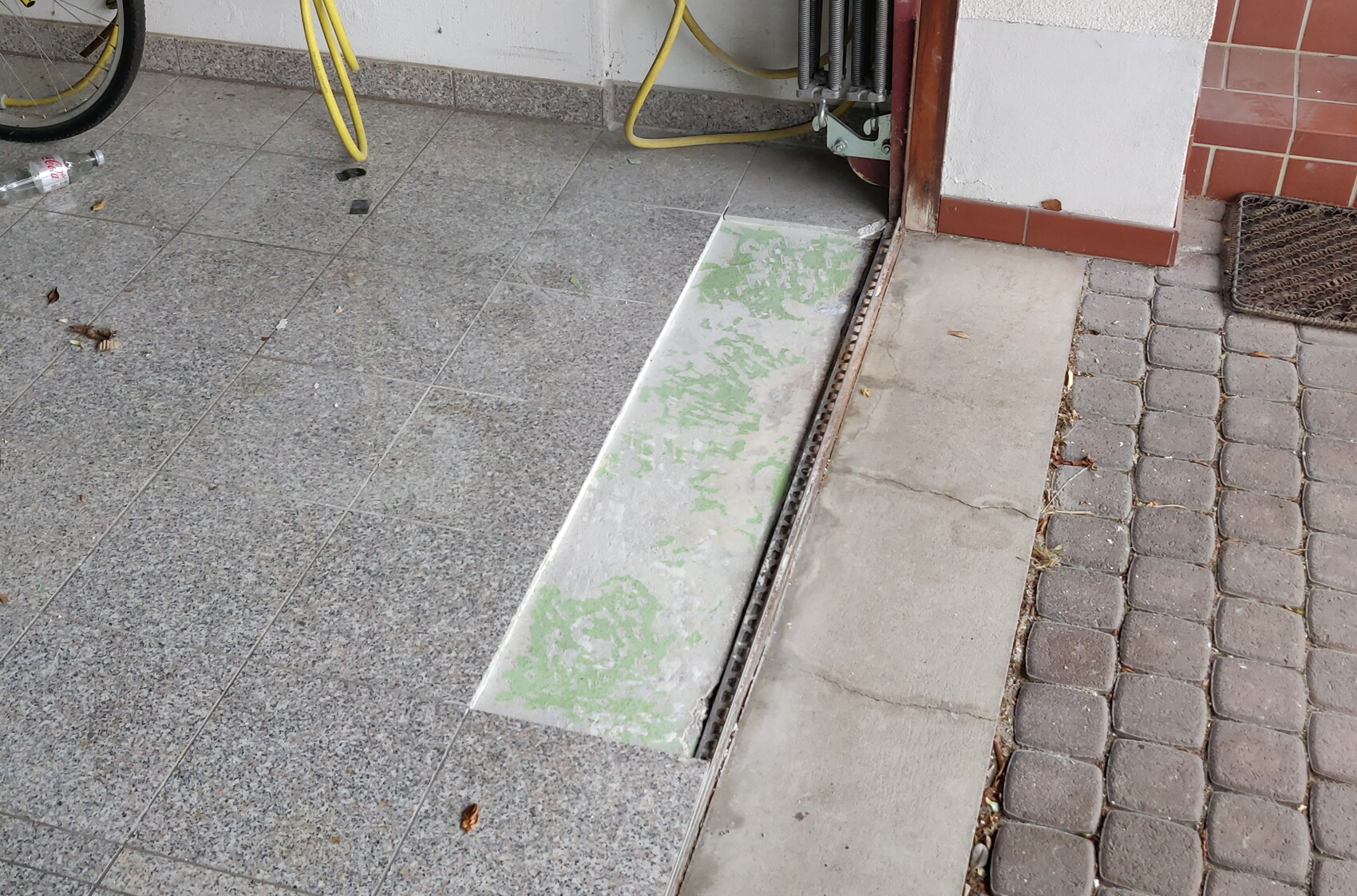 Exterior area with damaged floor tiles, drainage strip and yellow hoses