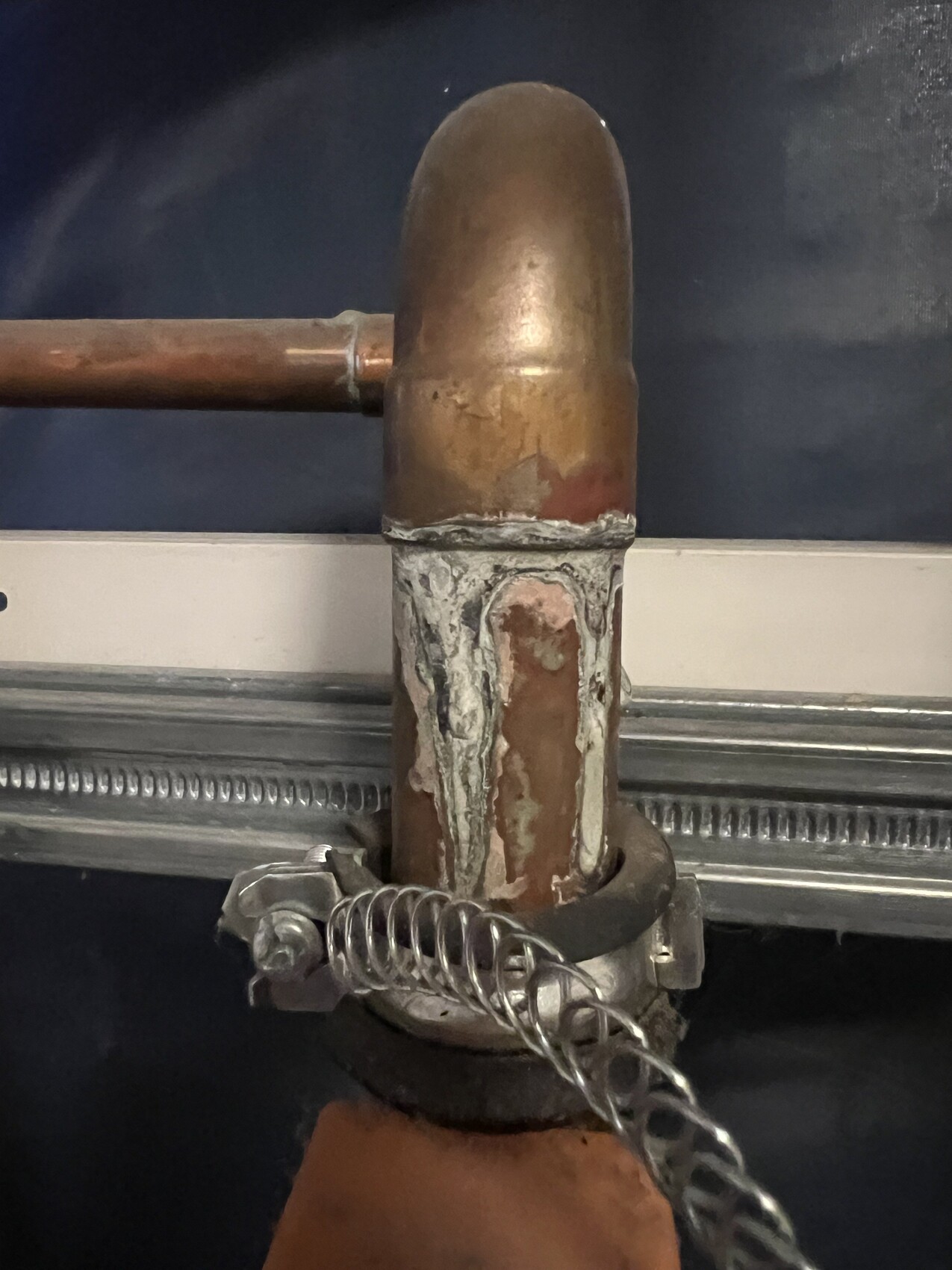 Corroded copper pipe connection with elbow piece, gray sealing paste and clamp with chain.
