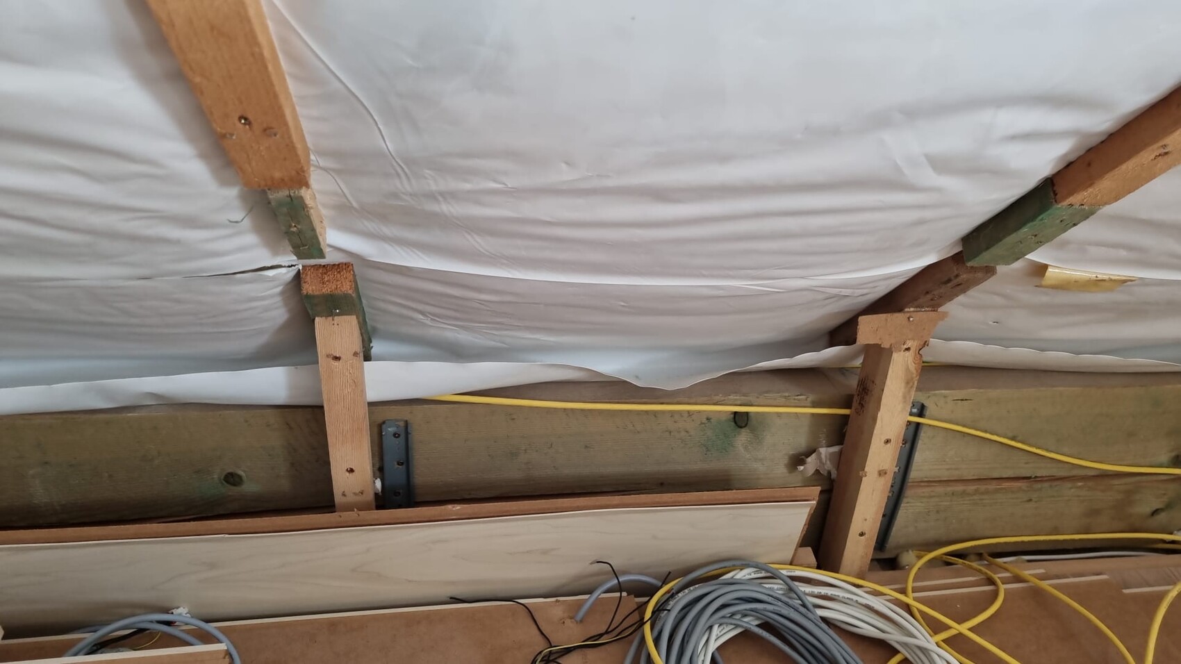 Indoor construction site with wooden beams, insulation foil, and loose cables