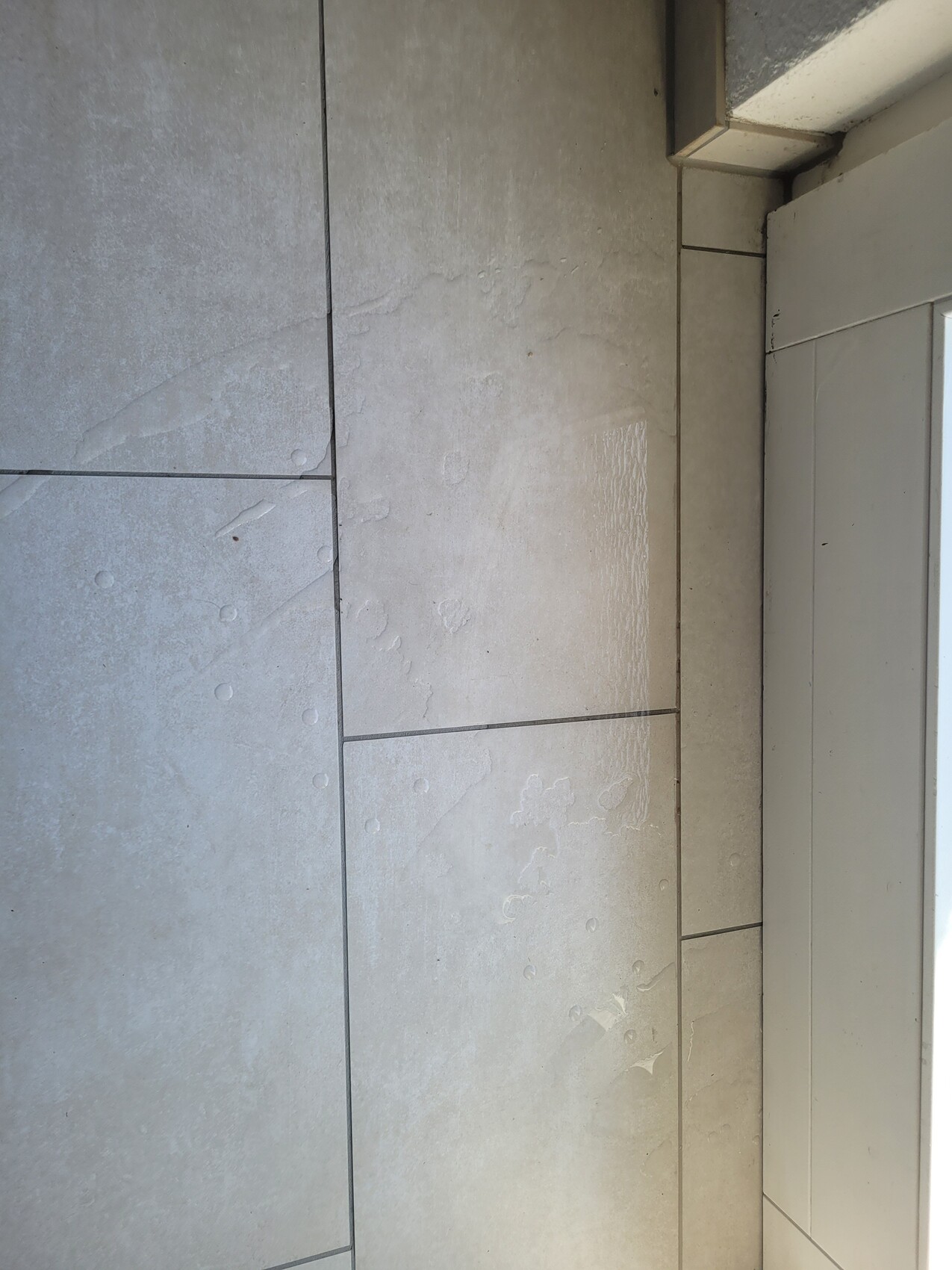 Gray tiled floor with moisture marks and puddles next to the door frame