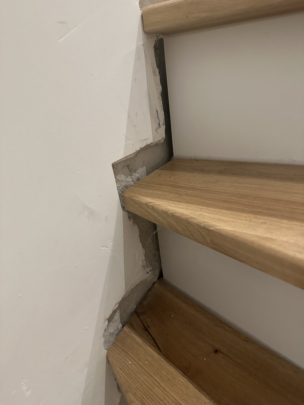 Wooden staircase at a damaged wall with exposed mortar behind the step.