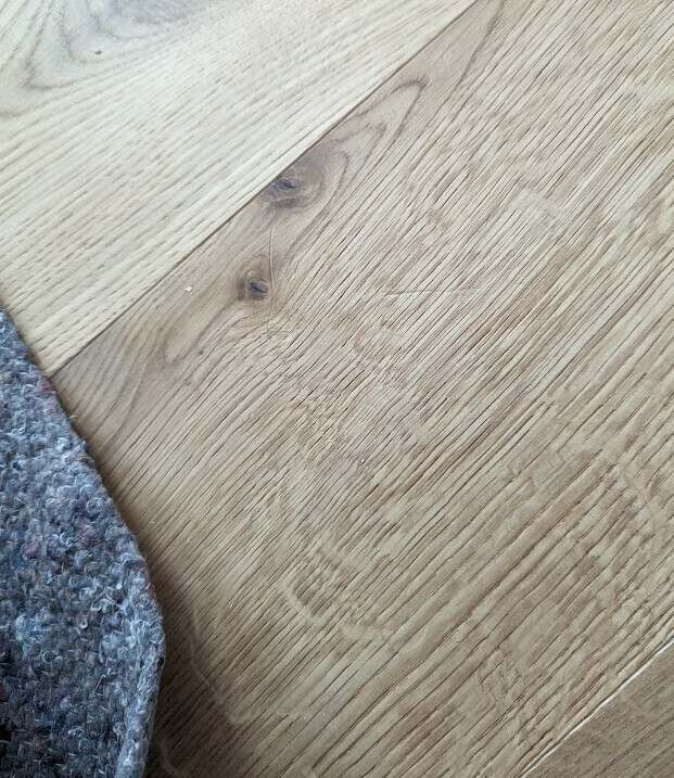 Light wooden floor with pronounced grain; carpet edge in the lower left corner.