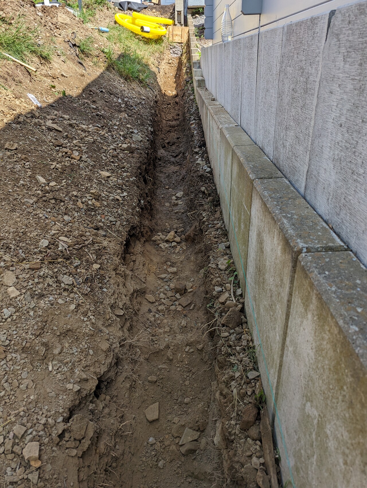 Tiefer Graben neben der Fundamentwand eines Hauses Erdreich und Kies entlang einer Betonblockwand.