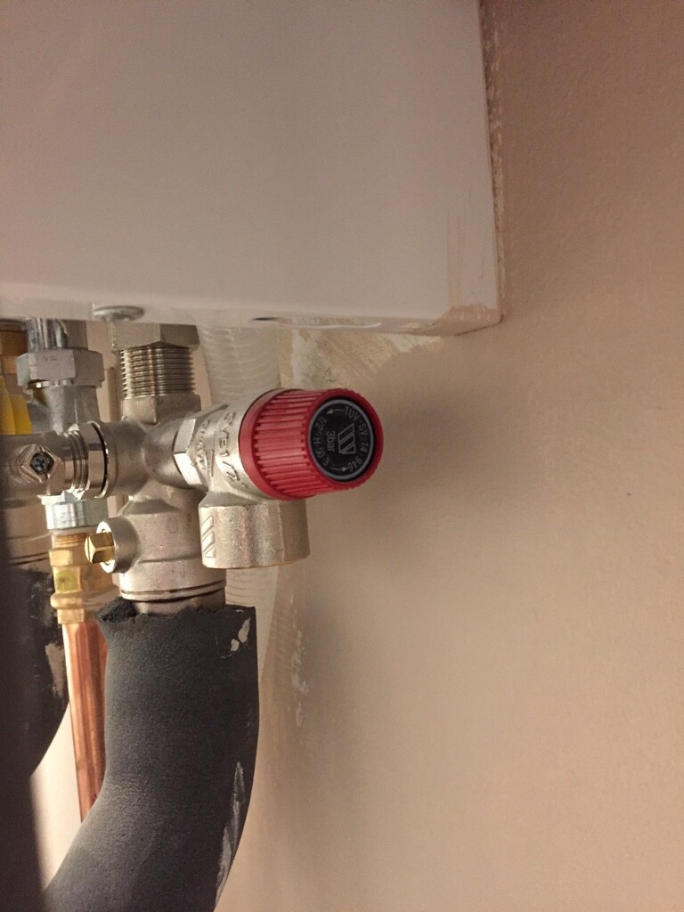 Close-up of a water shut-off valve with a red handle in a plumbing installation.