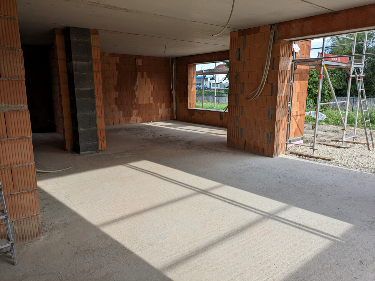 Unfinished interior made of red bricks, cables hanging from the ceiling; scaffolding visible outside.