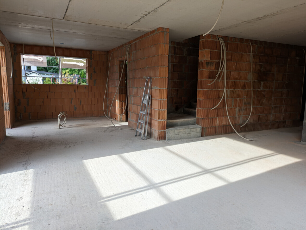 Interior of a shell construction with red brick walls, cables, ladder, and window opening.