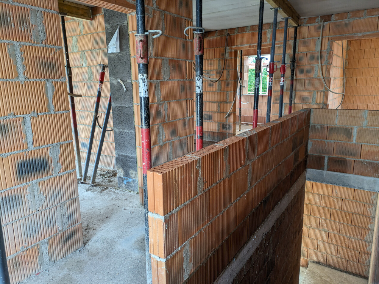 Interior of a construction site with unfinished brick walls, red steel supports, and visible openings.