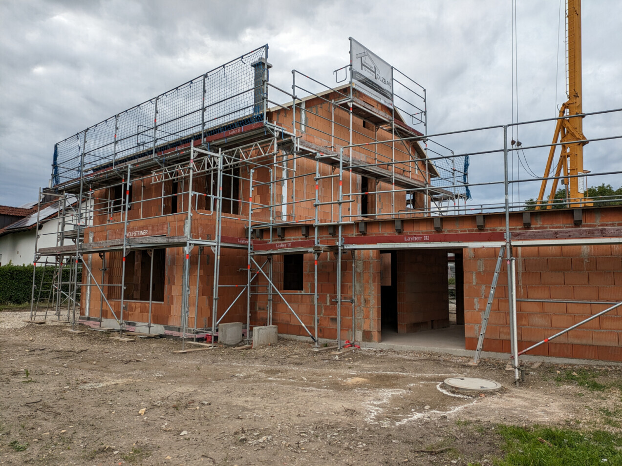 Two-story brick house in shell construction, surrounding scaffolding and construction crane on the right.