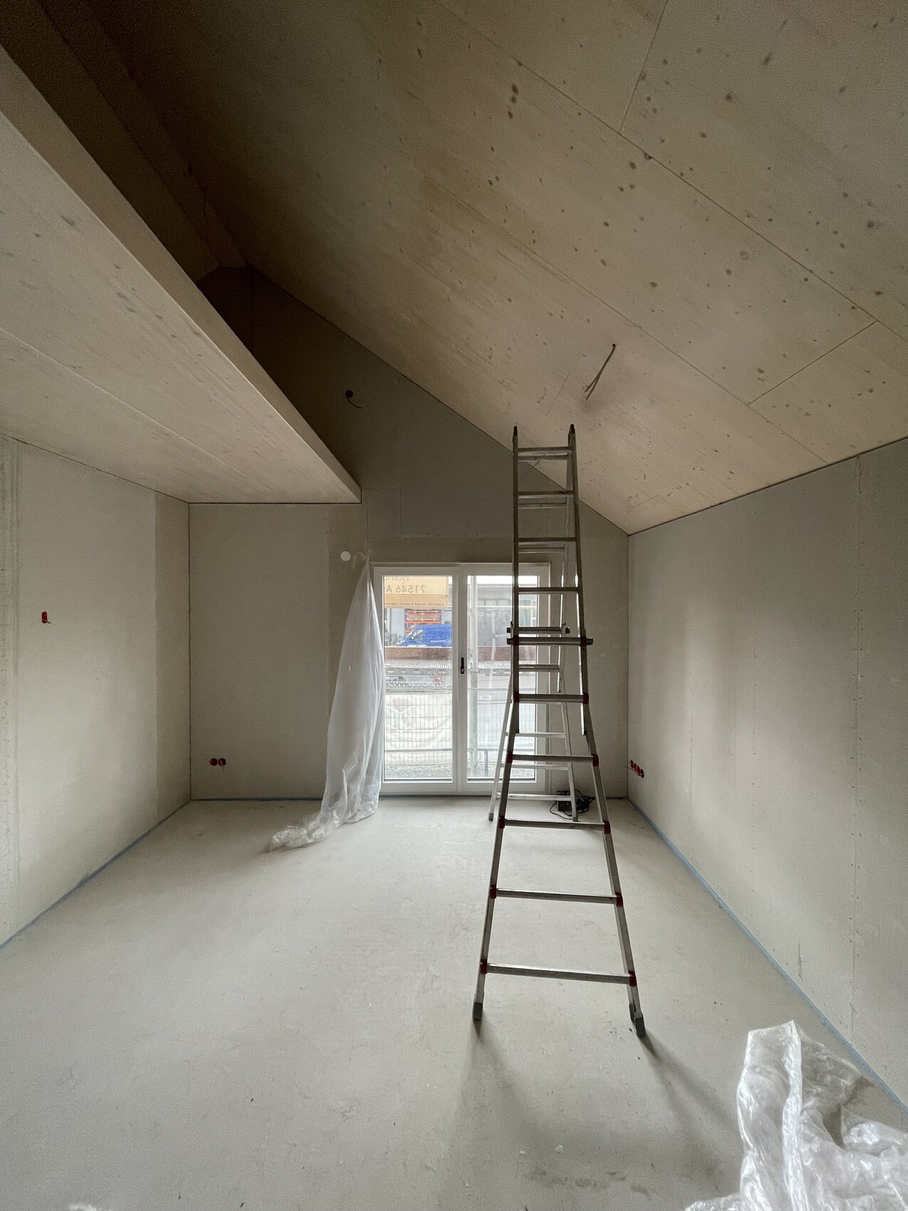 Unrenovierter Raum mit schräger Decke, Leiter in der Mitte, Fenster mit Plastikfolie.