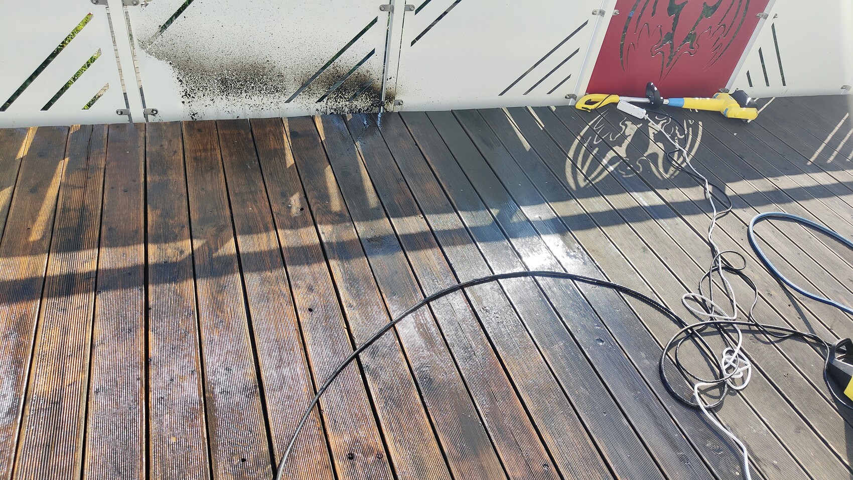 Wet wooden decking terrace; hose cable, pressure washer at the edge, red graphic wall.