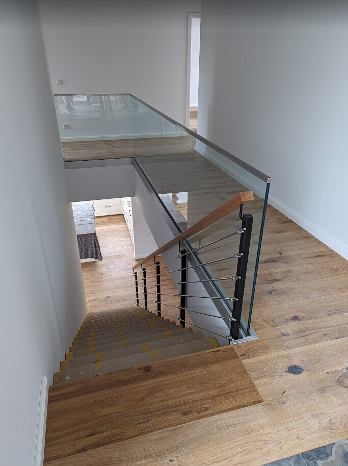 Modern staircase with glass and wooden railing, wooden floor, open stairwell to multiple levels.