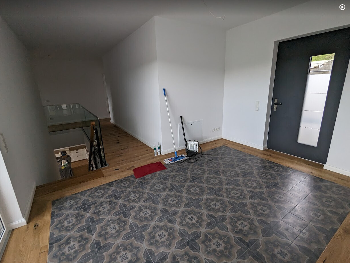 Bright entrance area with dark gray door, patterned tiled floor, and cleaning tools.