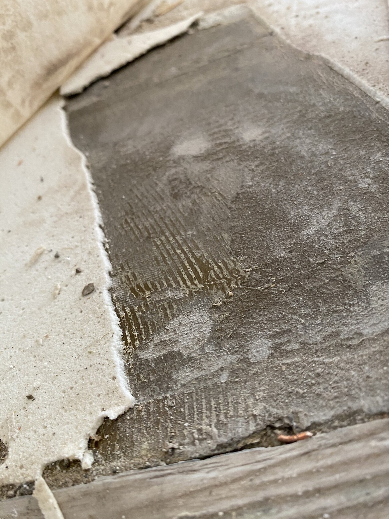 Close-up of a rough concrete surface with trowel marks and crumbling tile edge.