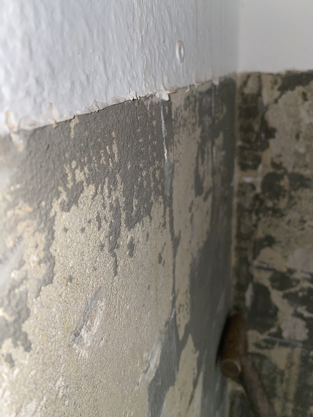 Corner of a plastered wall with peeling paint and rough concrete surface.