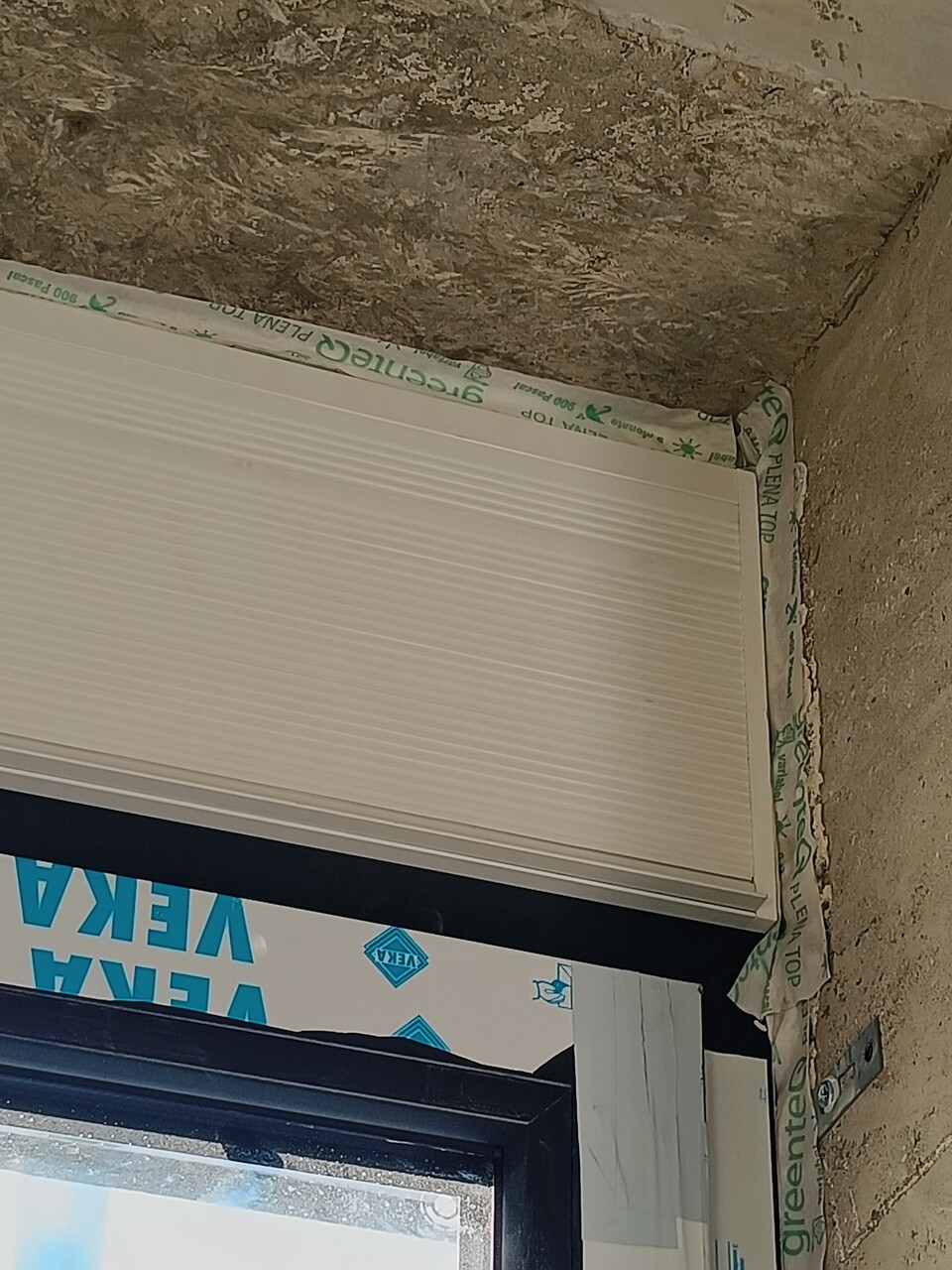 White roller shutter in window frame, construction foil around the window, rough shell.