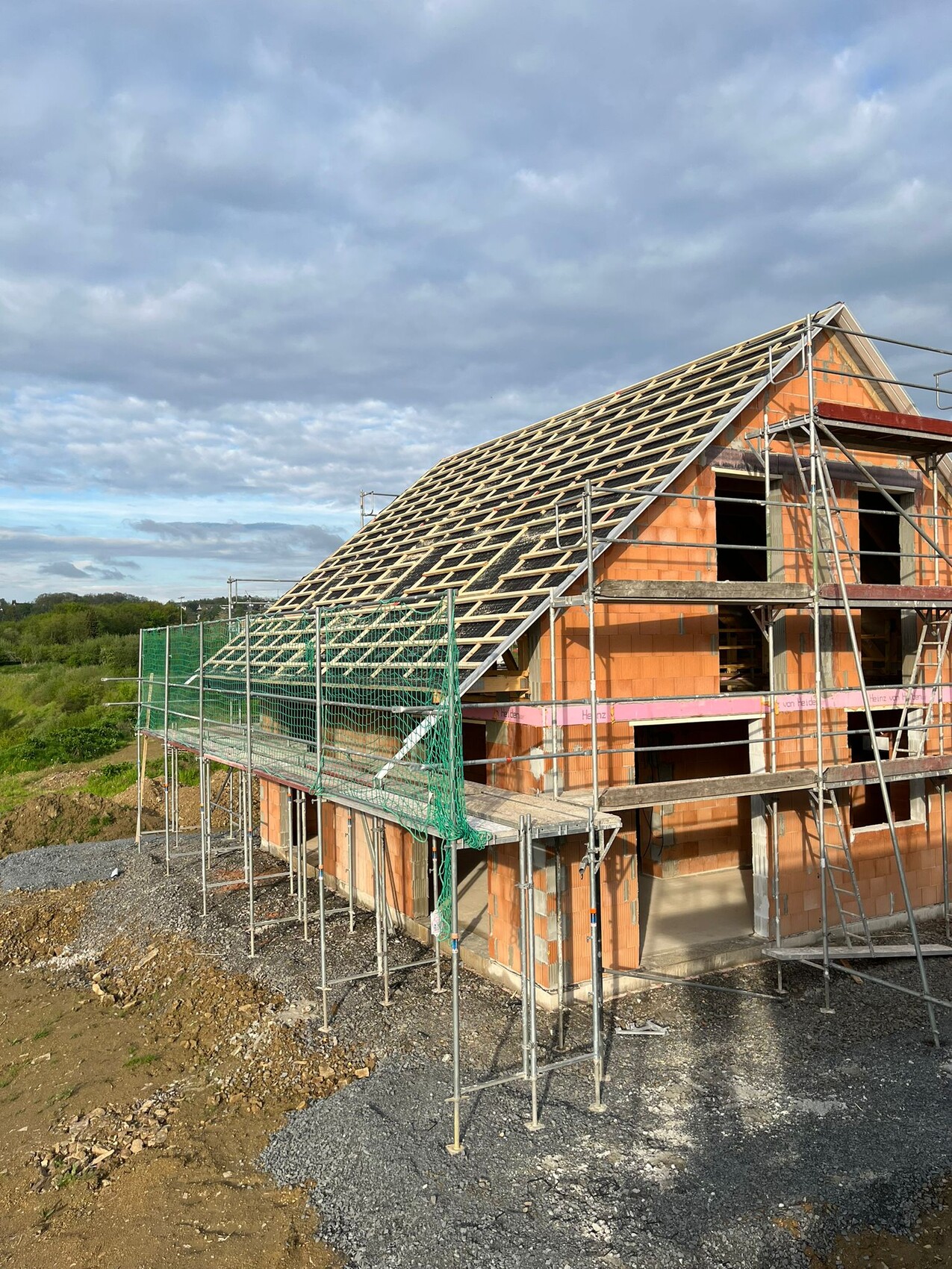 Shell of a house with wooden roof structure, scaffolding, and protective netting.