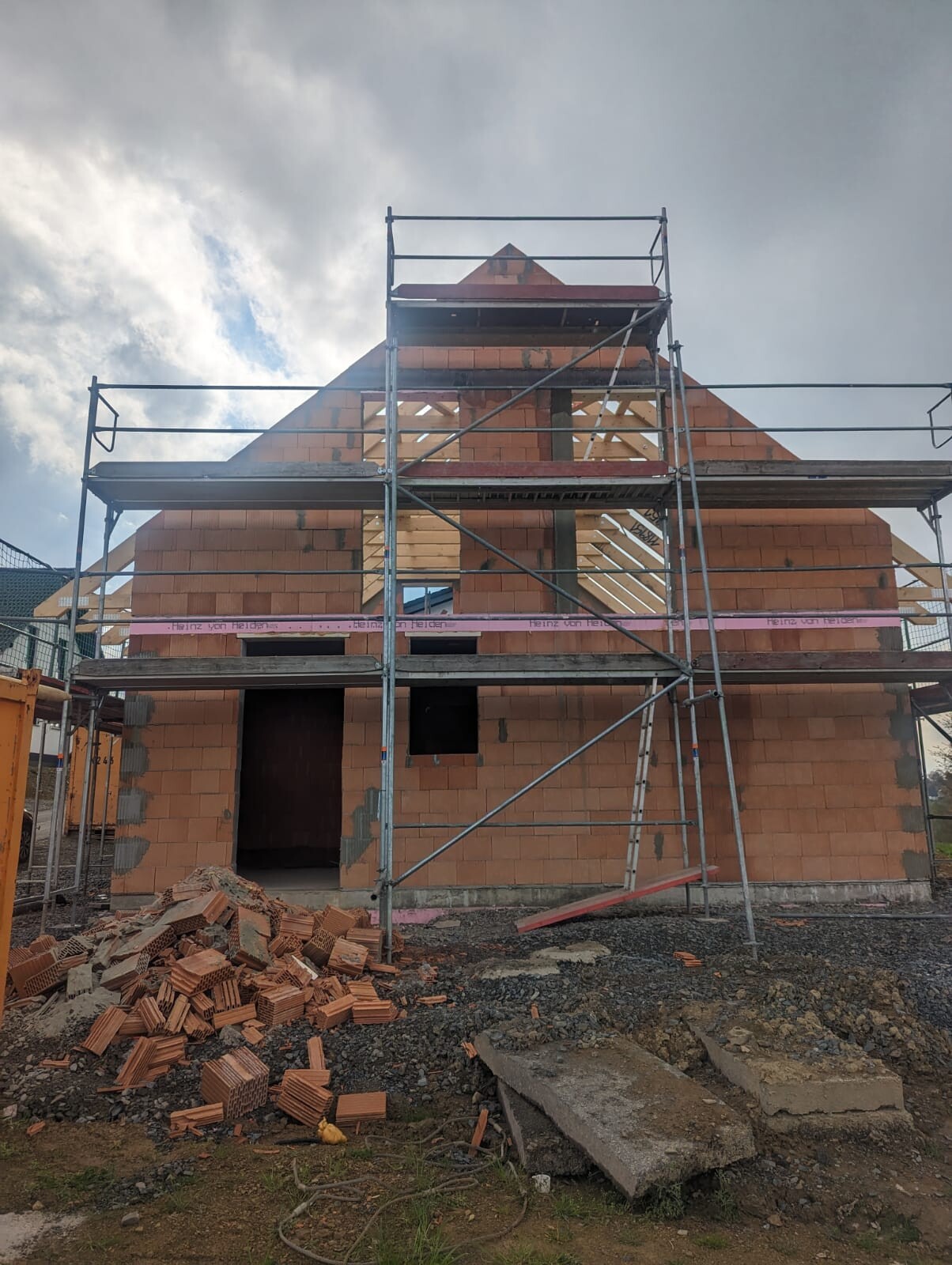 Shell of a red brick house with scaffolding; window openings, bricks lying on the ground.