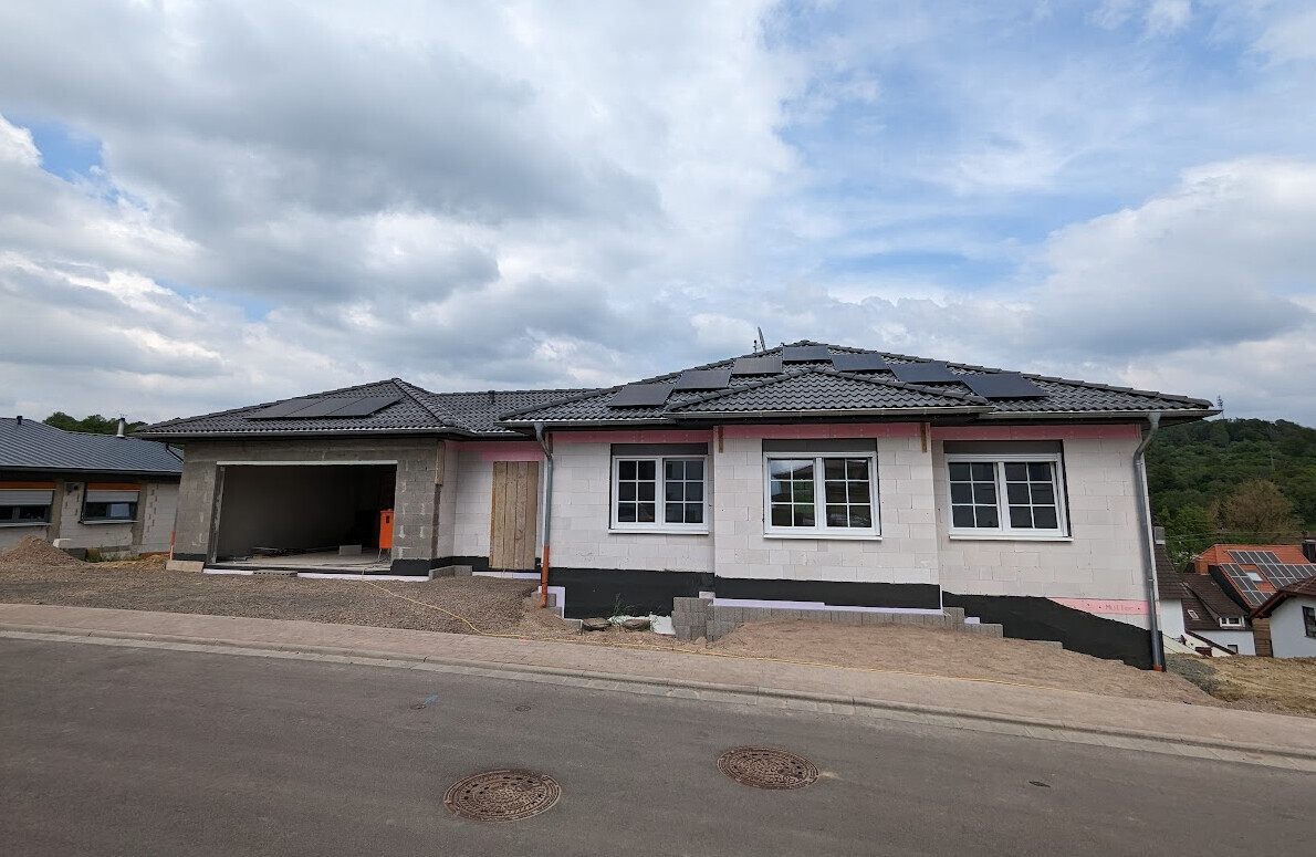Einfamilienhaus im Bau mit Solarmodulen auf dem Dach, offene Garage, Straße davor.
