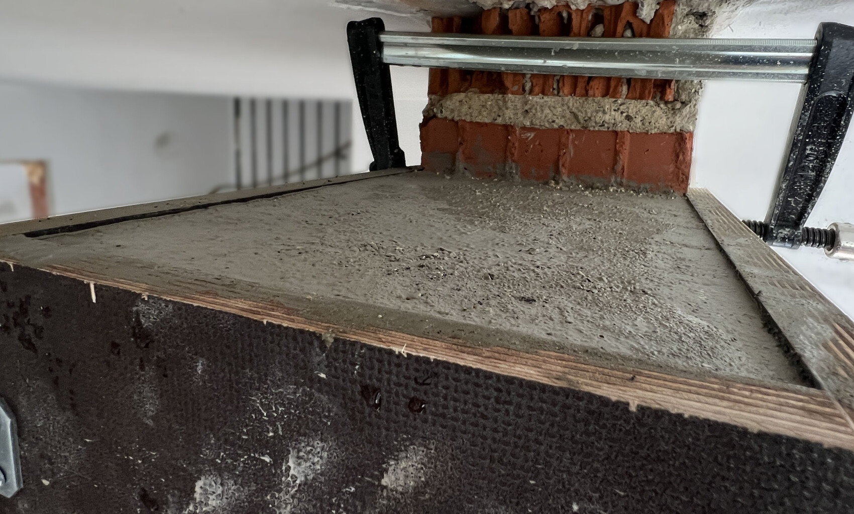 Interior shell construction: concrete floor on formwork, brick wall behind, metal clamp visible