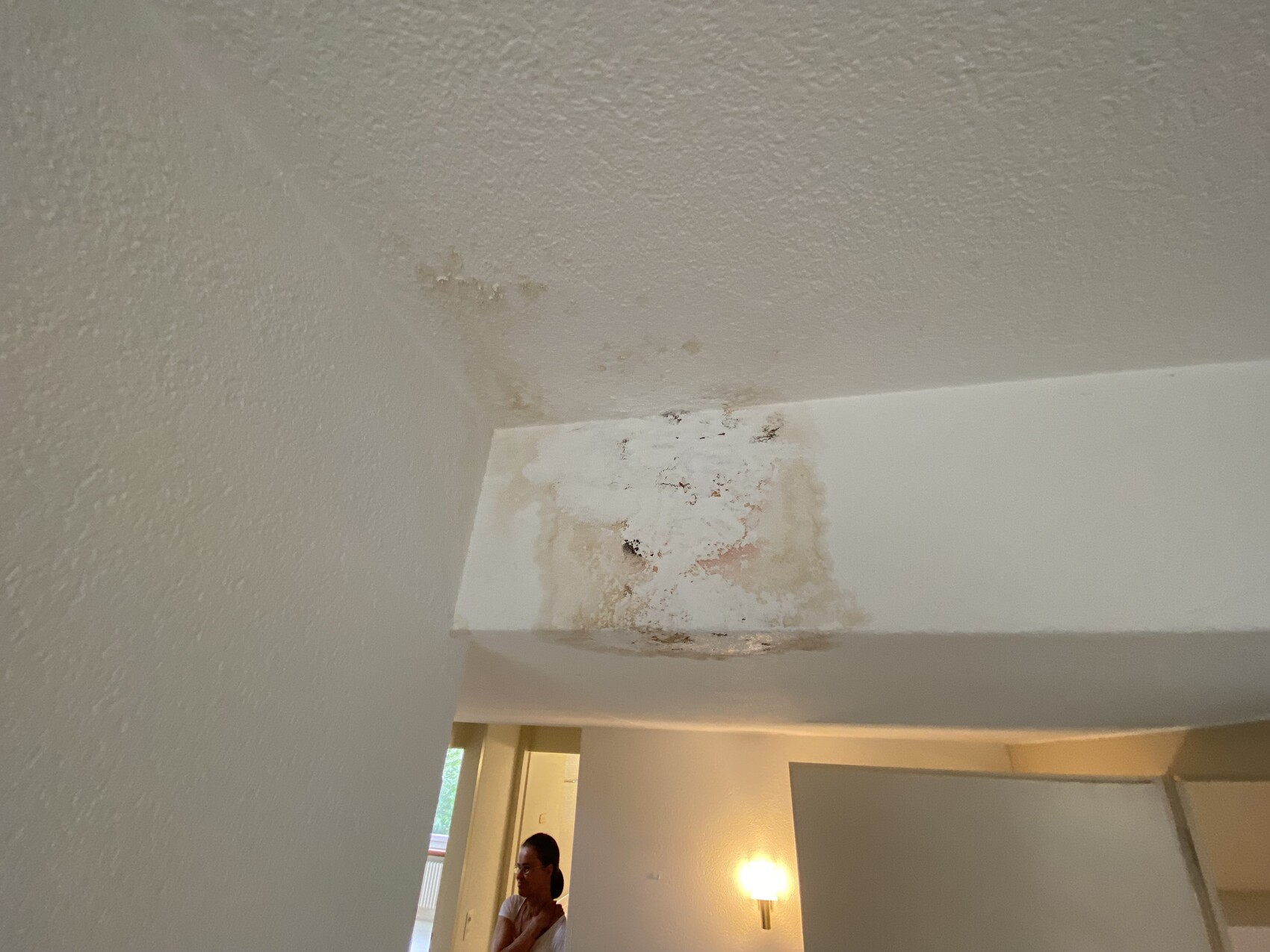 Ceiling patch with water stain and peeling paint above the door frame; a person is visible in the background.