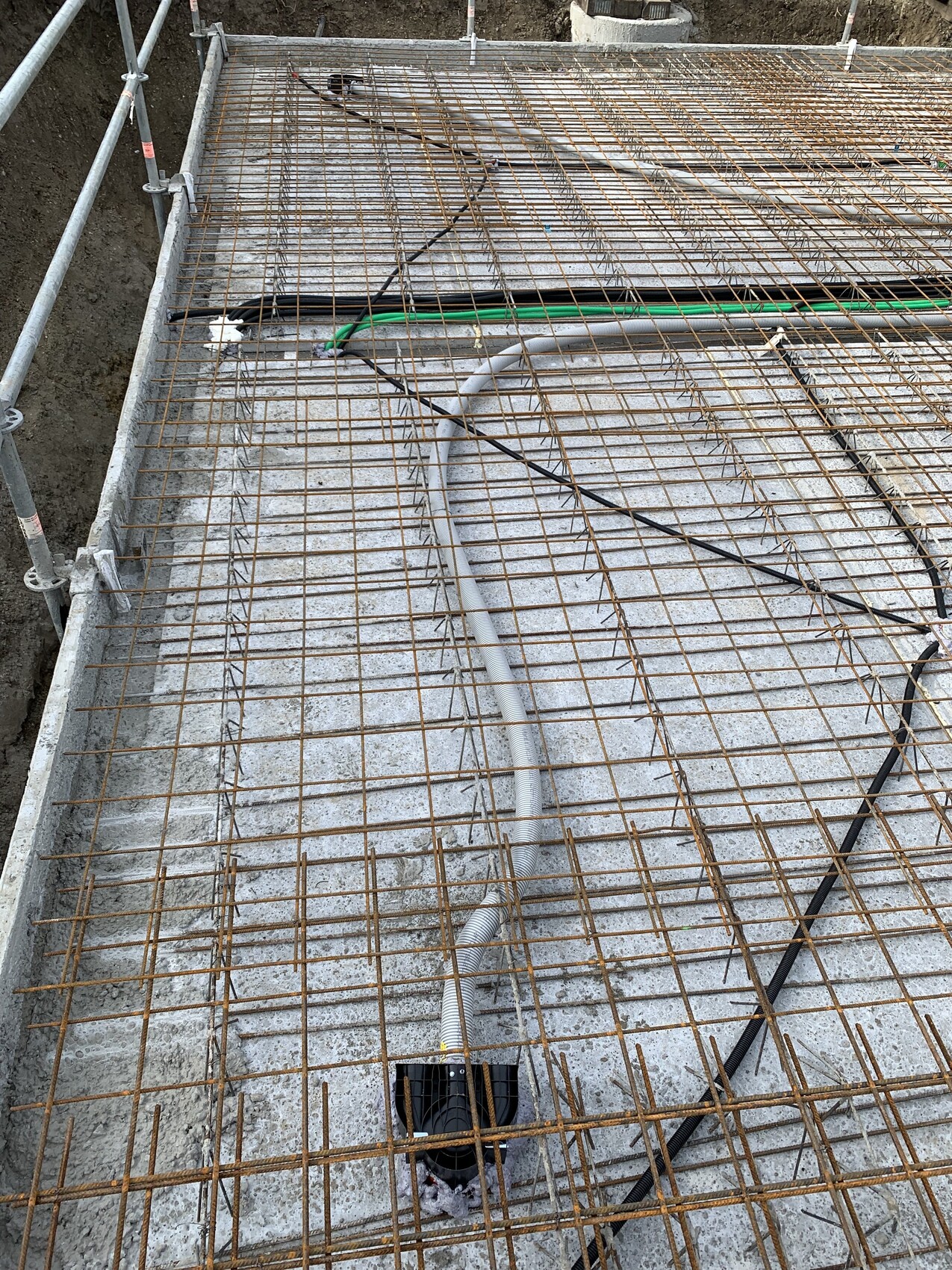 Bewehrungsstahl-Gitter auf Betonfundament; Schlauchleitungen und grüne Wasserleitung verlaufen.