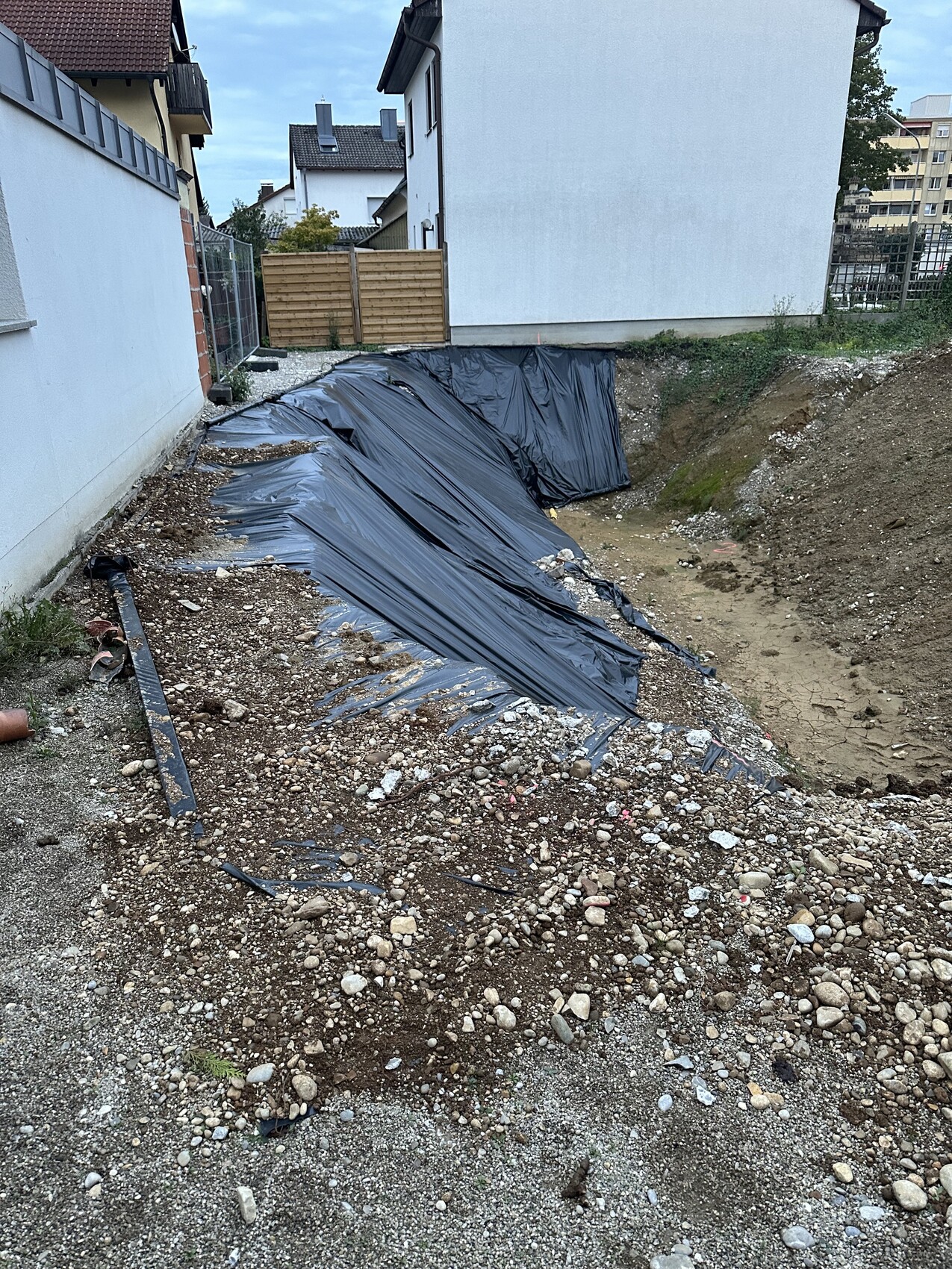 Excavation pit with black sealing membrane, gravel and soil; building in the background