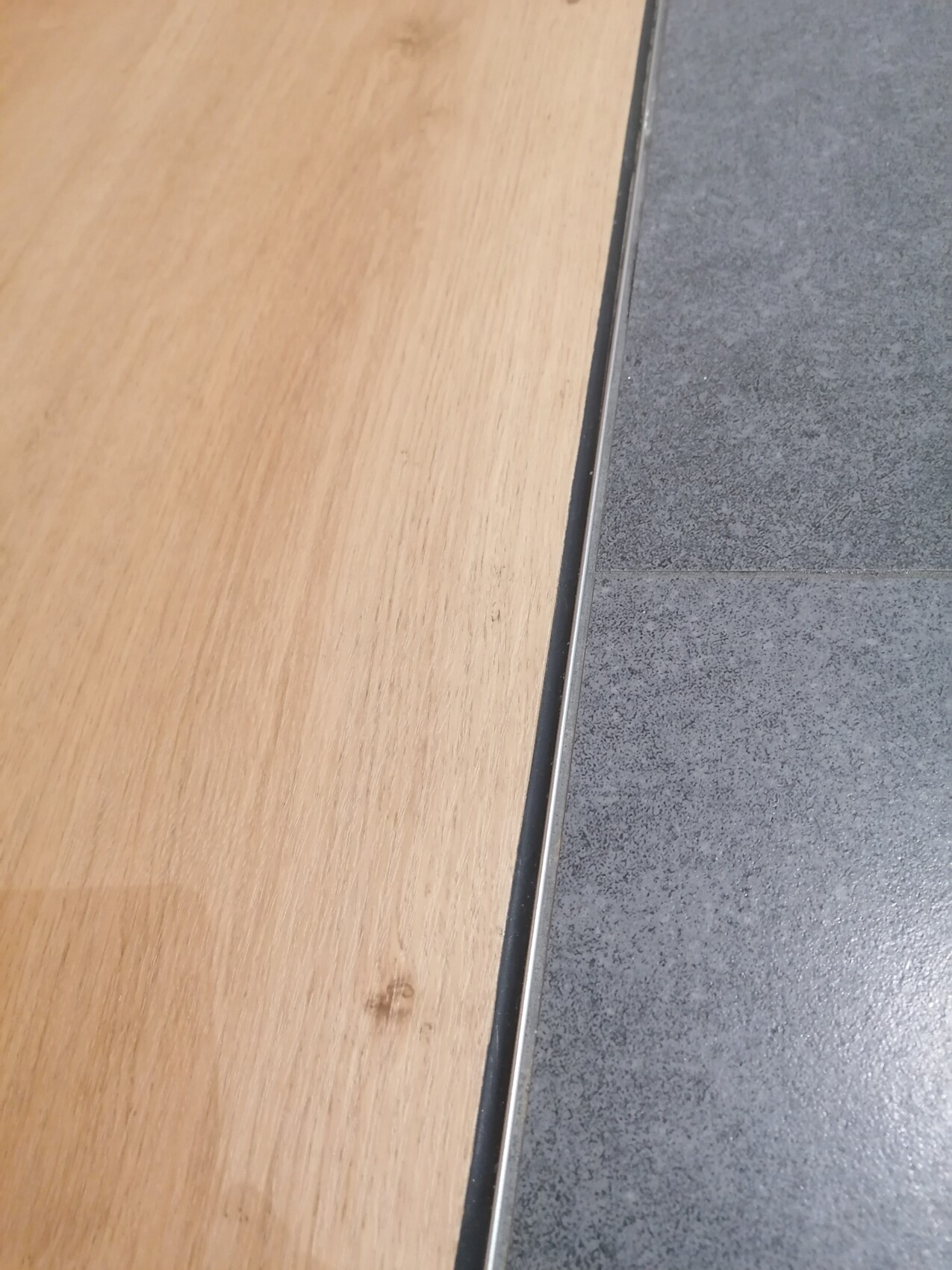 Transition between wooden floor on the left and gray tiled floor on the right, metal edge.
