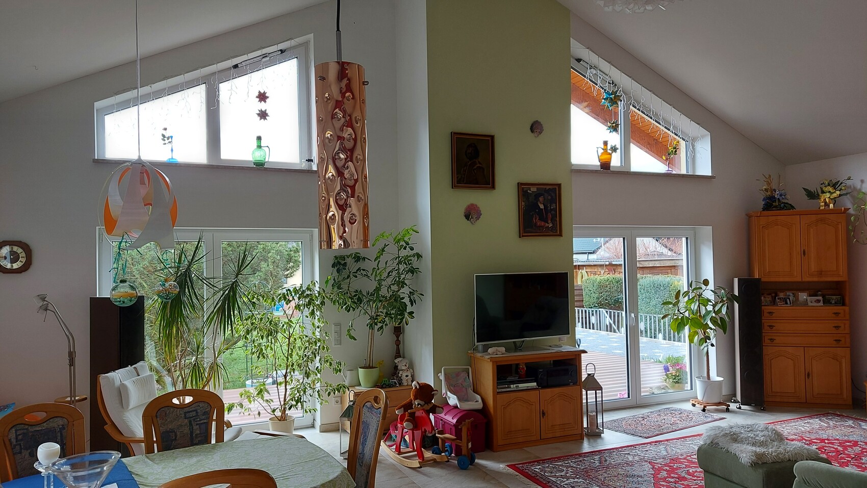 Bright living room with many potted plants, TV on wooden cabinet, green wall, window to the garden