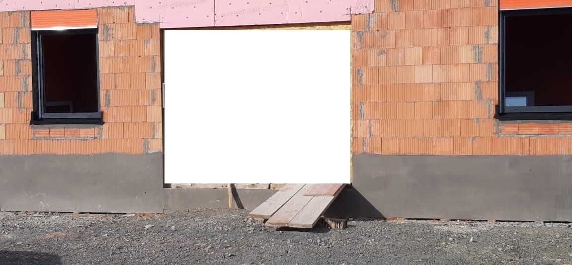 Baustellenwand aus Ziegeln, zwei Fenster, zentrale Türöffnung mit Holzrampe