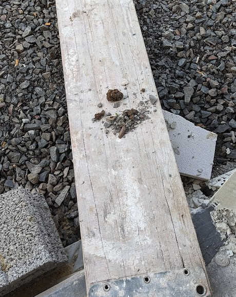 Wooden board on gravel surface with clumps of dirt and construction material around it