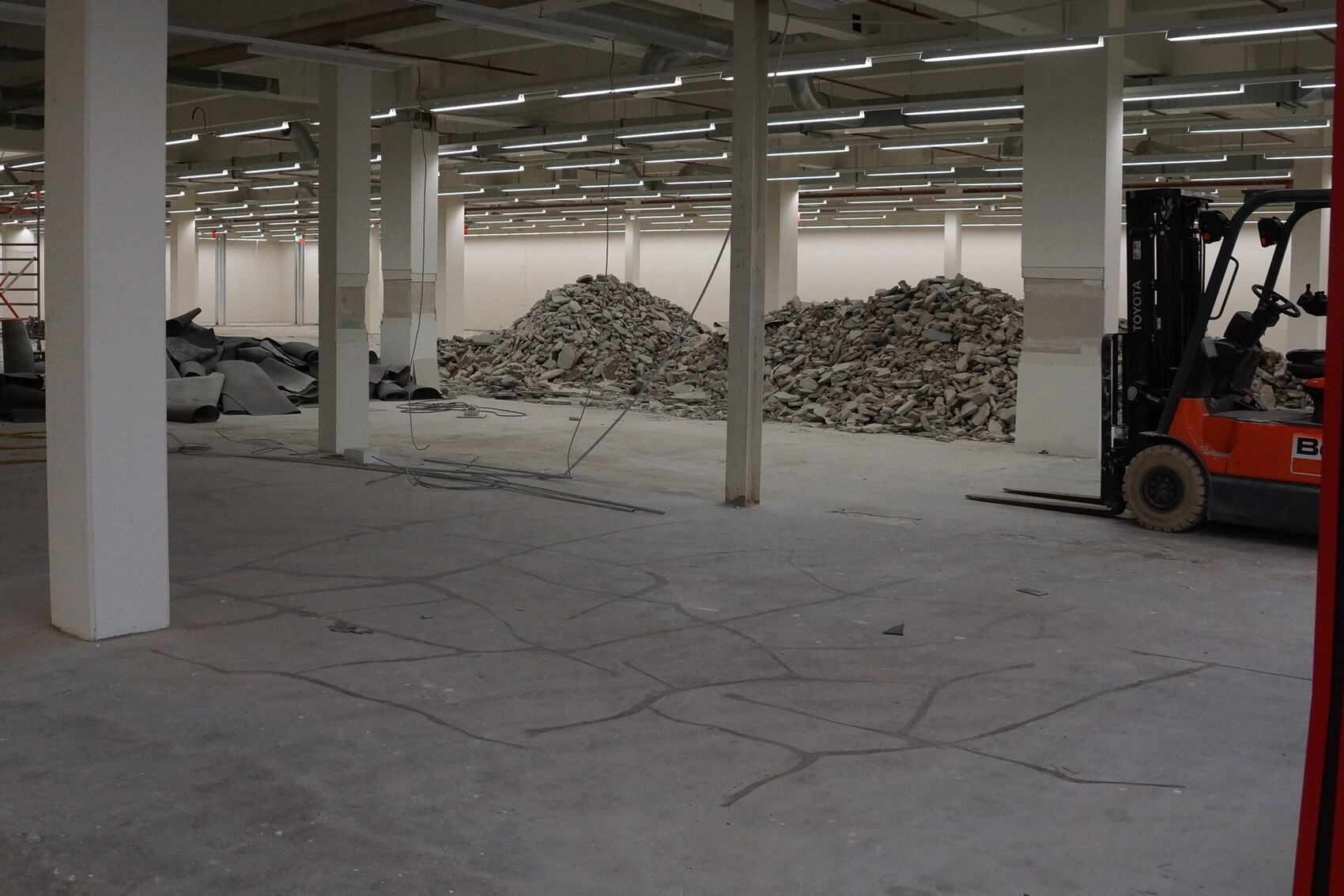 Large construction hall with columns, debris pile in the center and forklift on the right.
