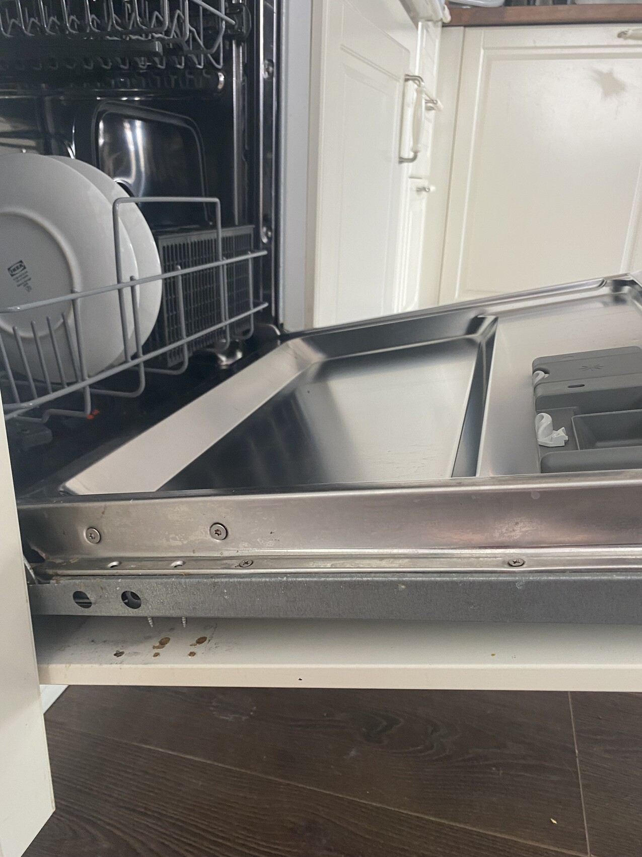 Open dishwasher interior: left plate rack with plates, stainless steel bottom.
