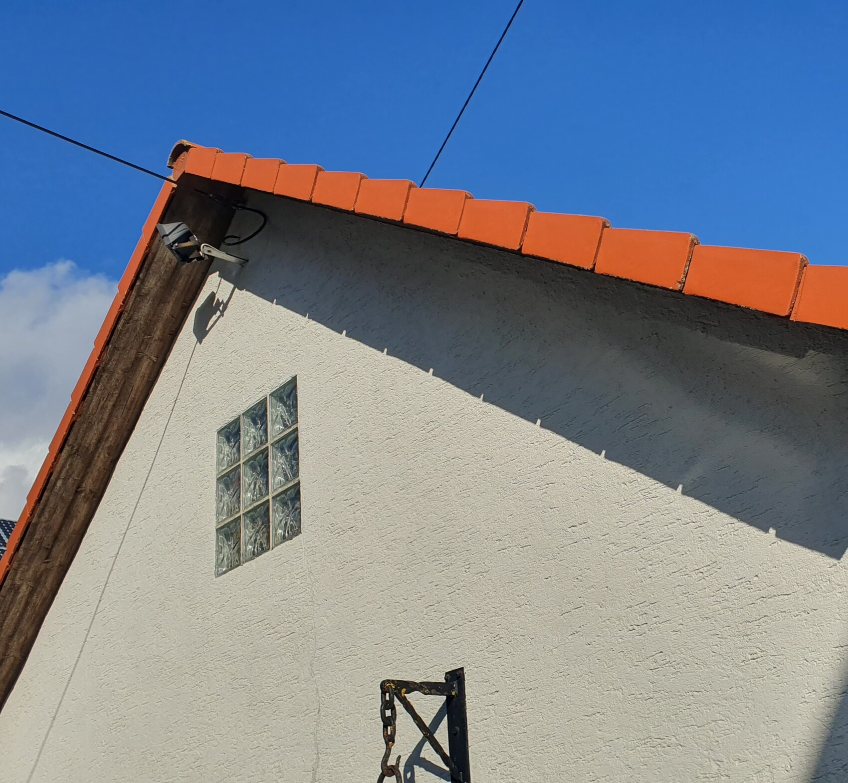 White house wall with orange tiled roof, security camera, wire rope and glass block window
