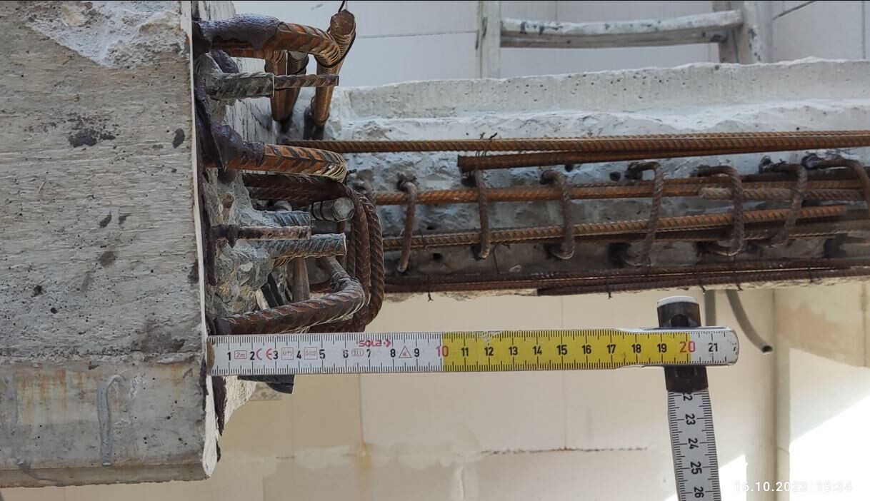 Rusty steel reinforcement bars in a concrete wall; a tape measure lying horizontally above them.