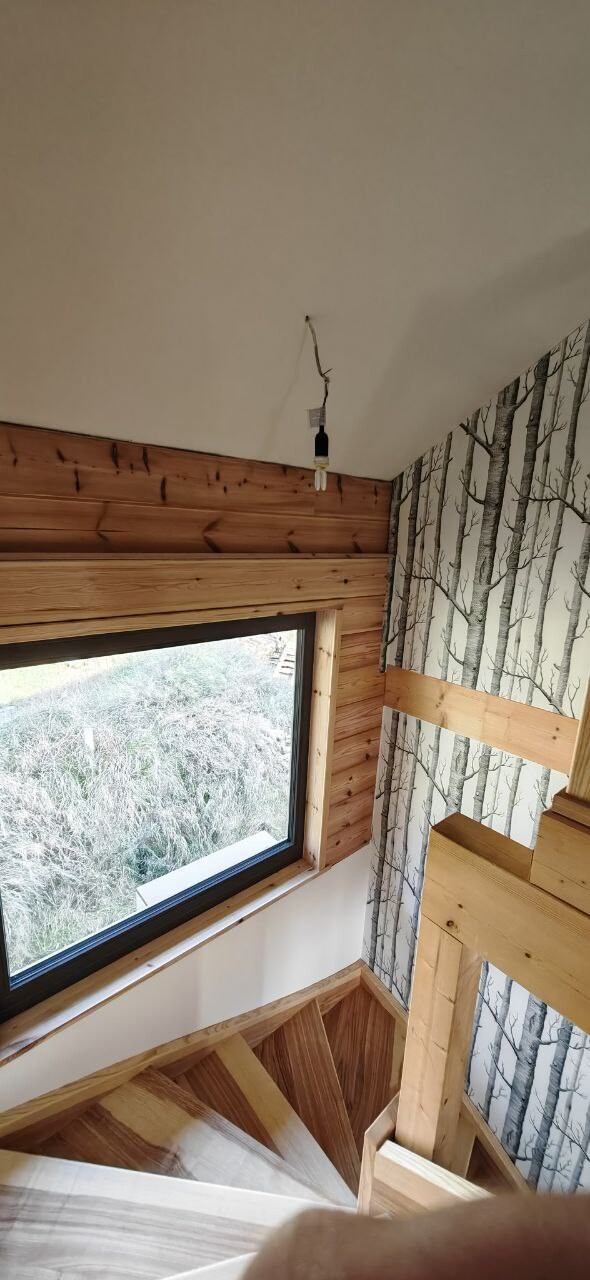 Wooden staircase in a bright interior, large window, tree bark wallpaper, hanging loose light fixture.