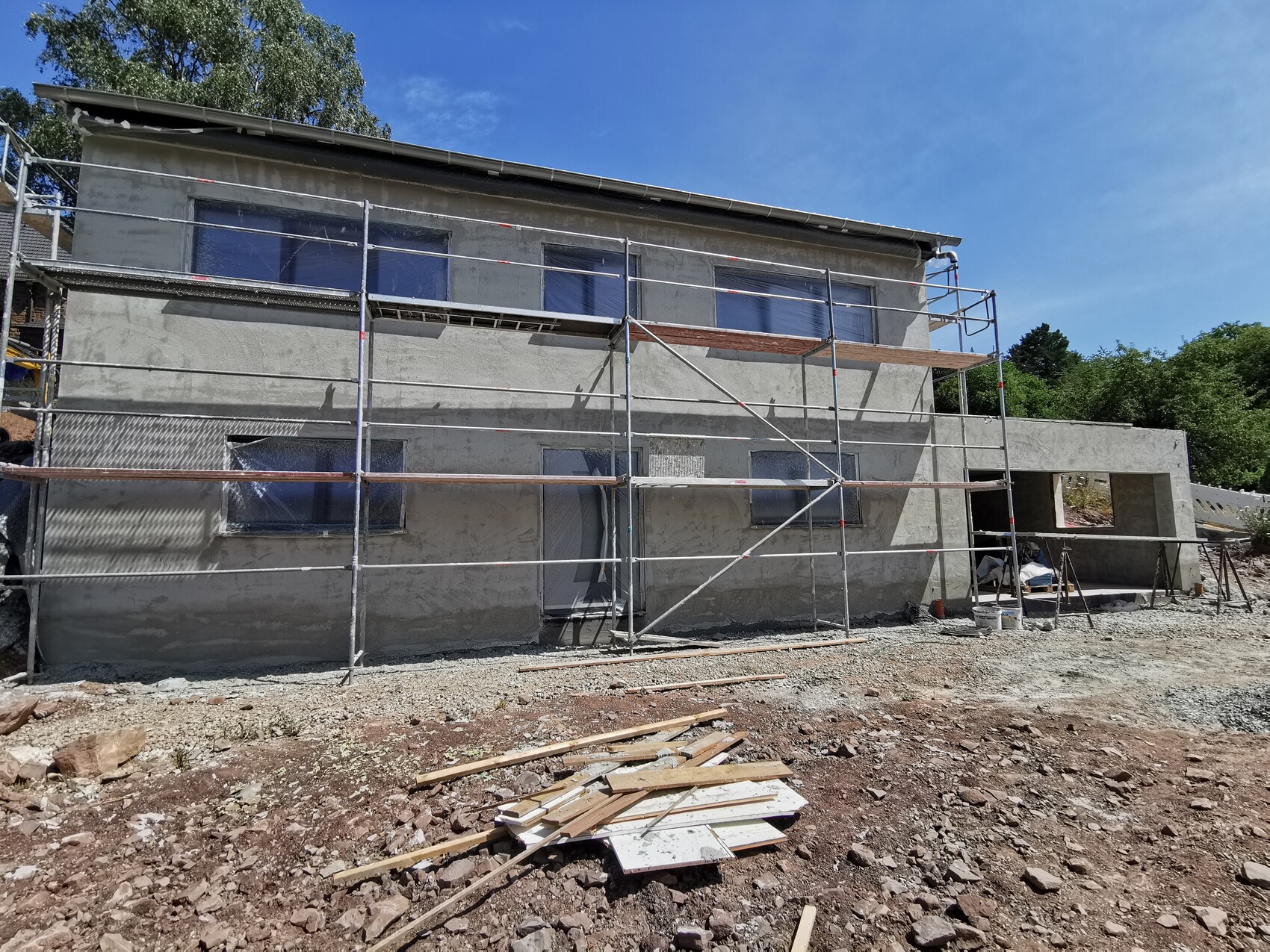 Two-story house with scaffolding, facade work, construction equipment, and gravel in the foreground
