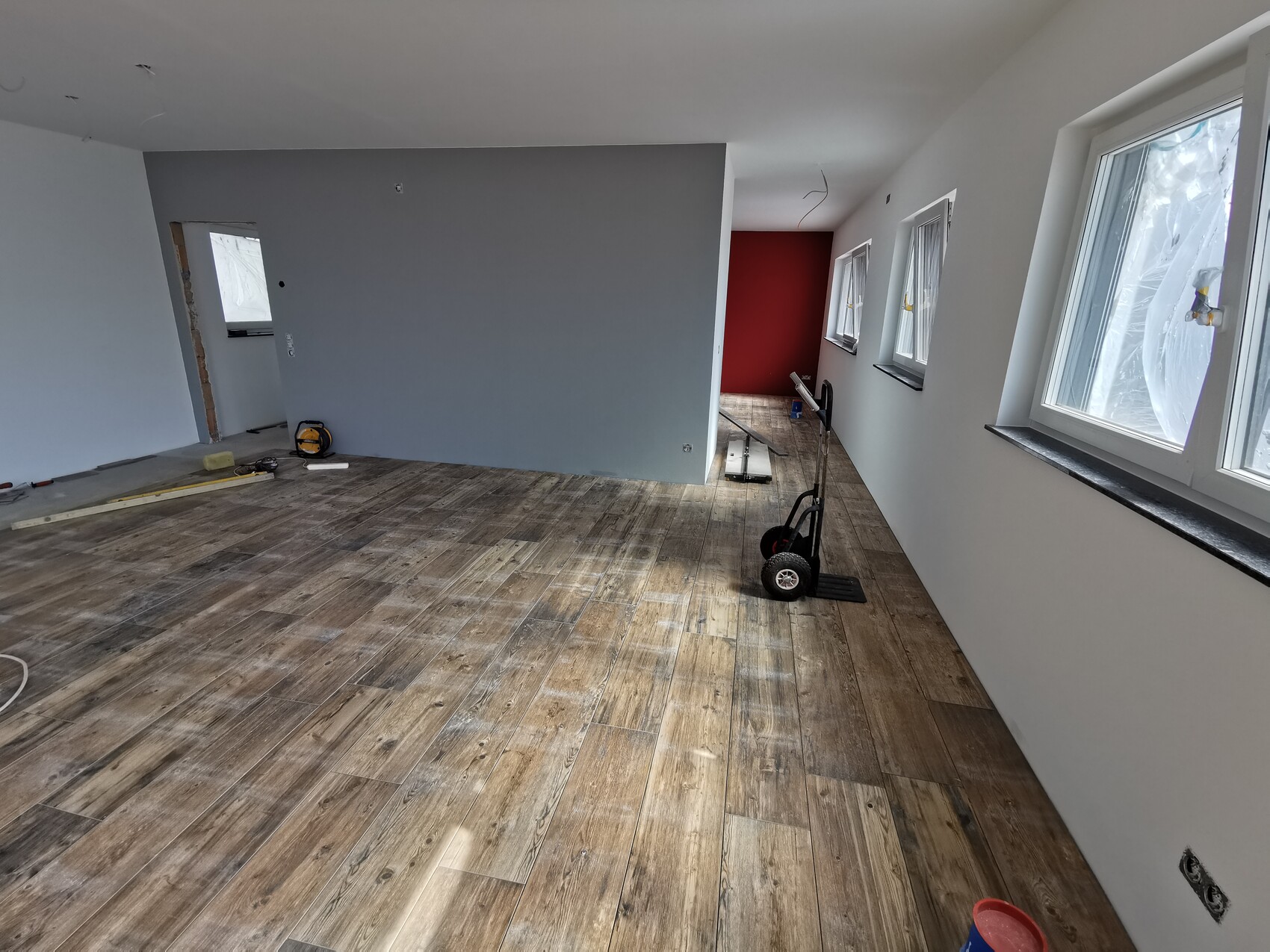 Renovation room with wood floor, gray accent wall, red background wall, and window front on the right.