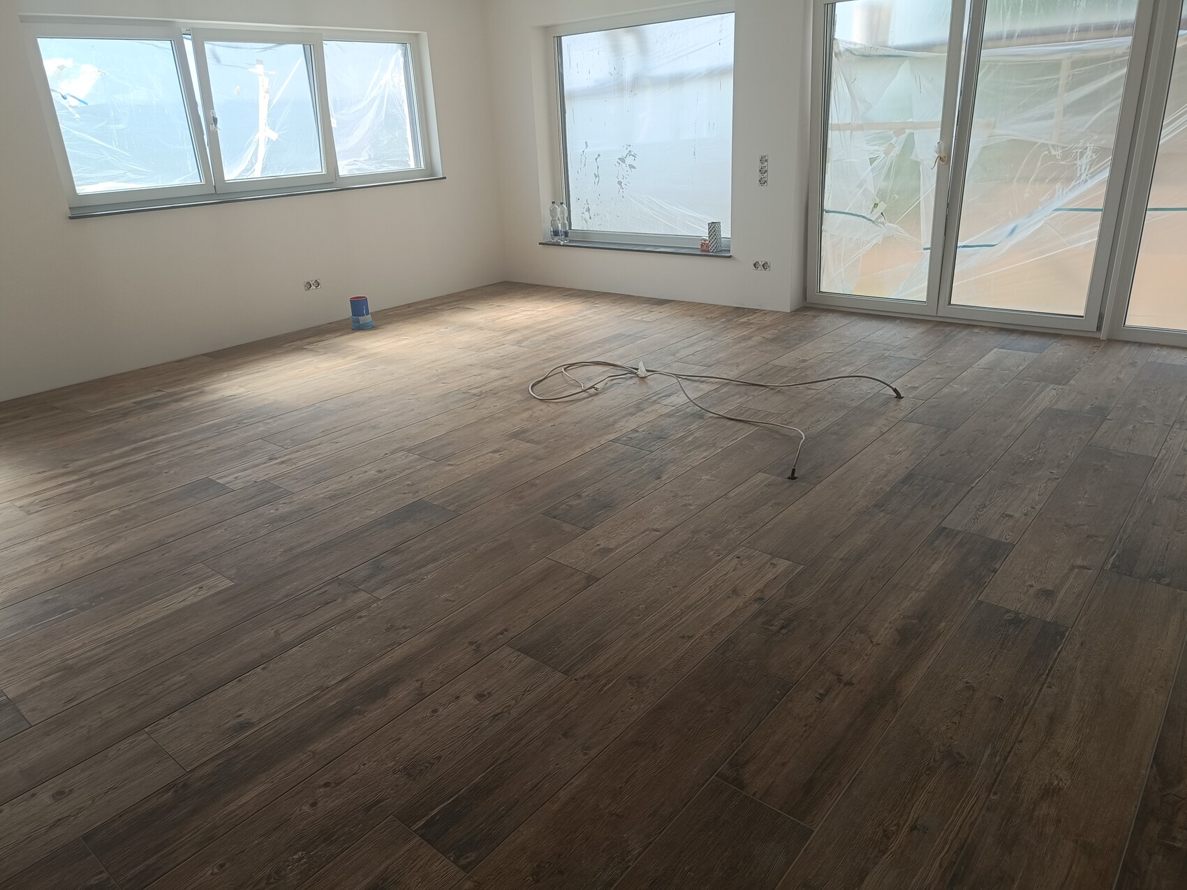 Bright empty room with wood laminate floor; window front behind plastic foil; cables on the floor
