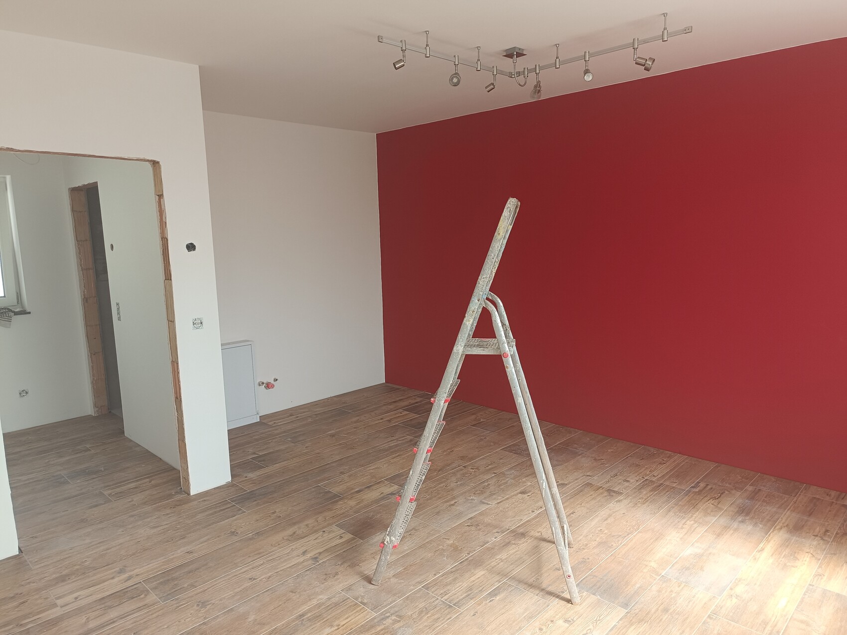 Room with red wall, a ladder on wooden floor, renovation work.