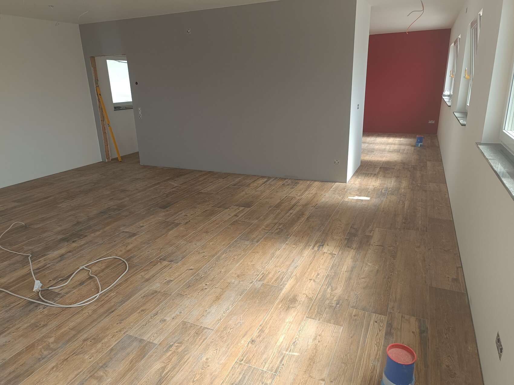 Renovated interior with wooden floor, gray walls and red accent wall at the back.