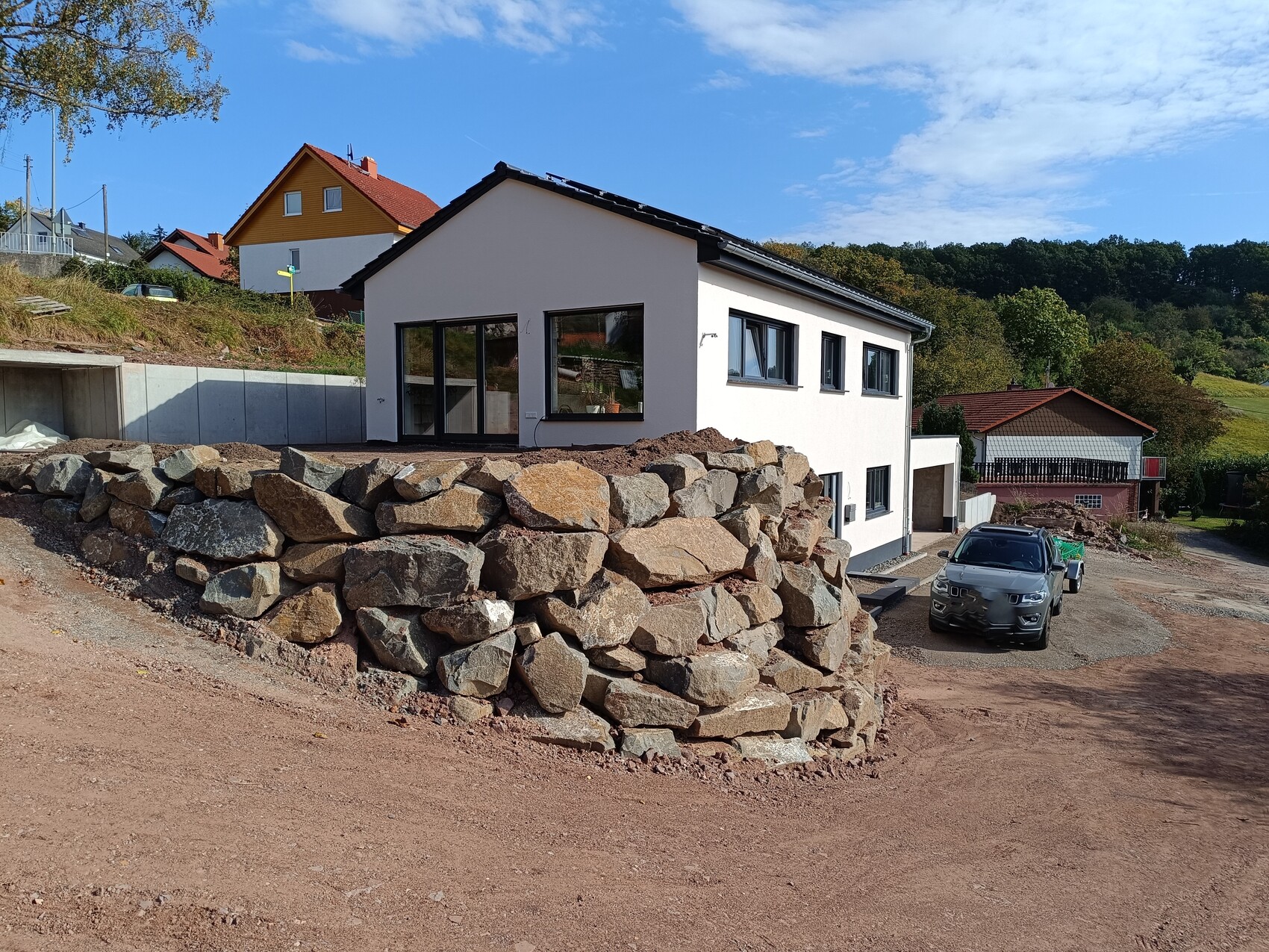 Modern white single-family house on a stone wall made of boulders, SUV in front.