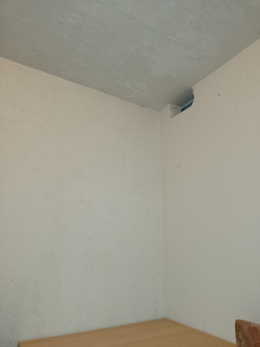 Empty room with white walls, gray ceiling, corner with opening and wooden table in foreground.