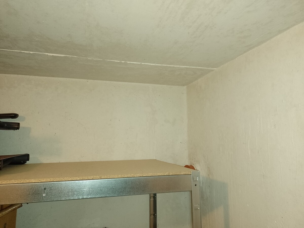 Basement storage room with concrete walls and ceiling; metal shelf below with items on it.