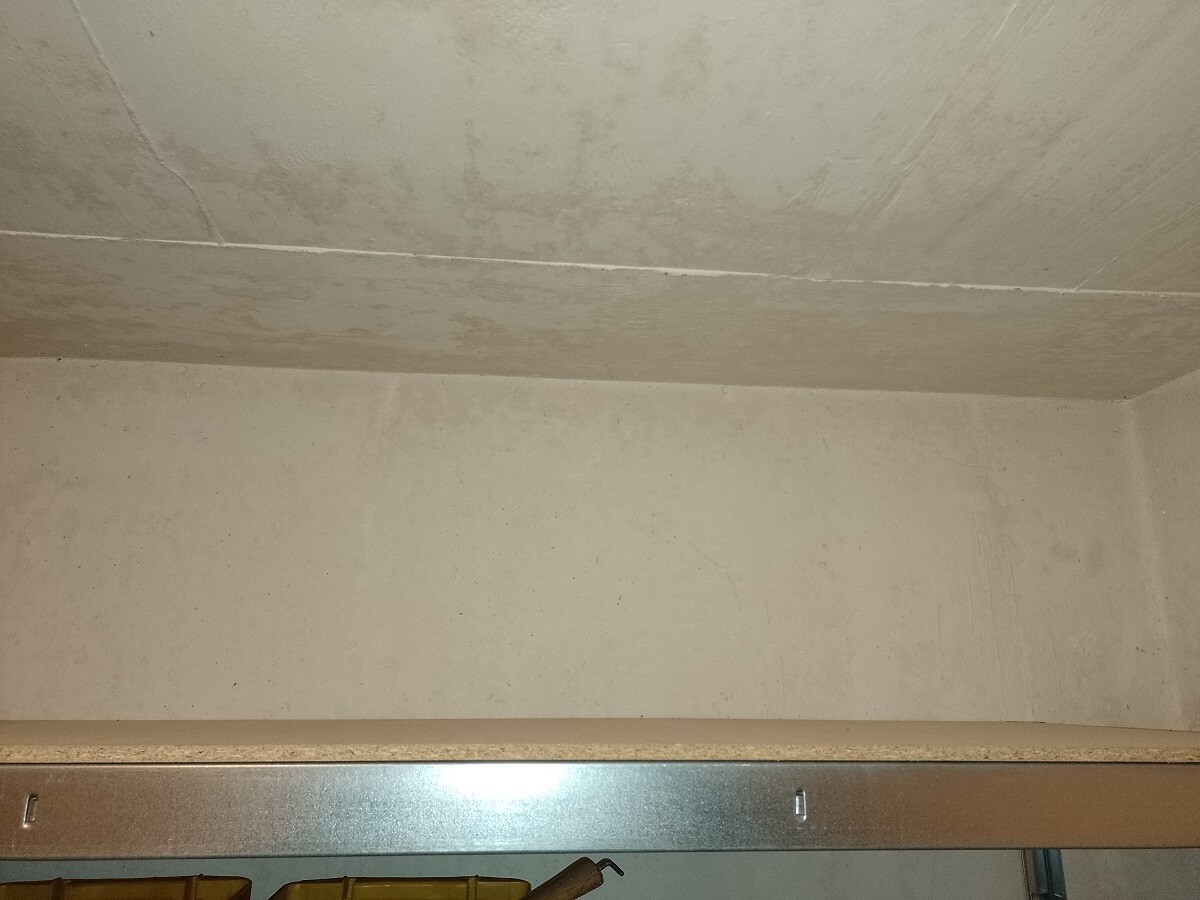 Empty basement room with gray concrete wall and ceiling, metal shelf below and yellow boxes.
