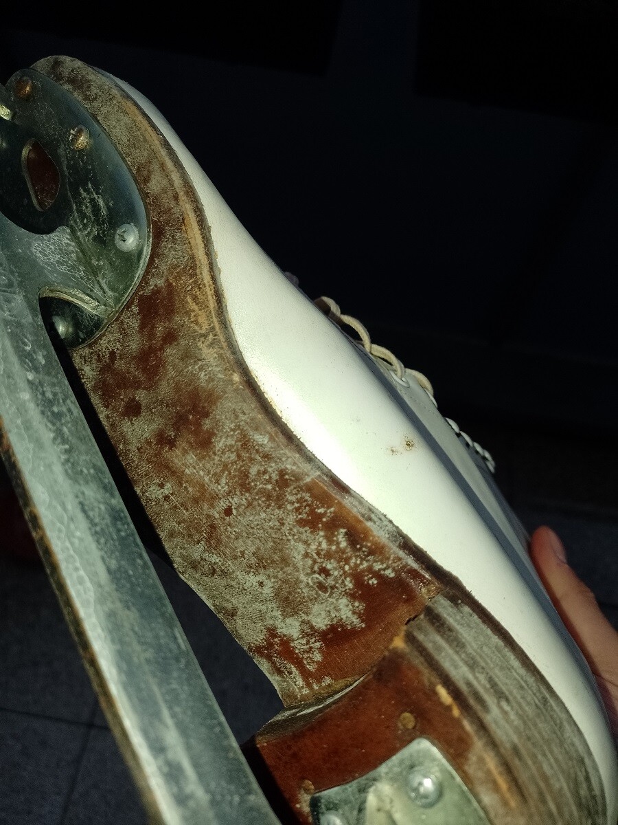 Close-up of rusty figure skating skate with white shoe and metal blade.
