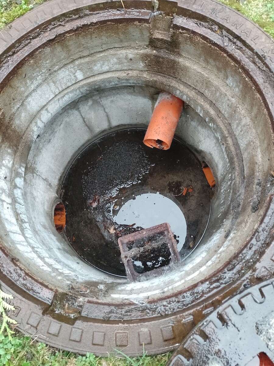 Open inspection shaft with black water and mud; an orange pipe extends into it.