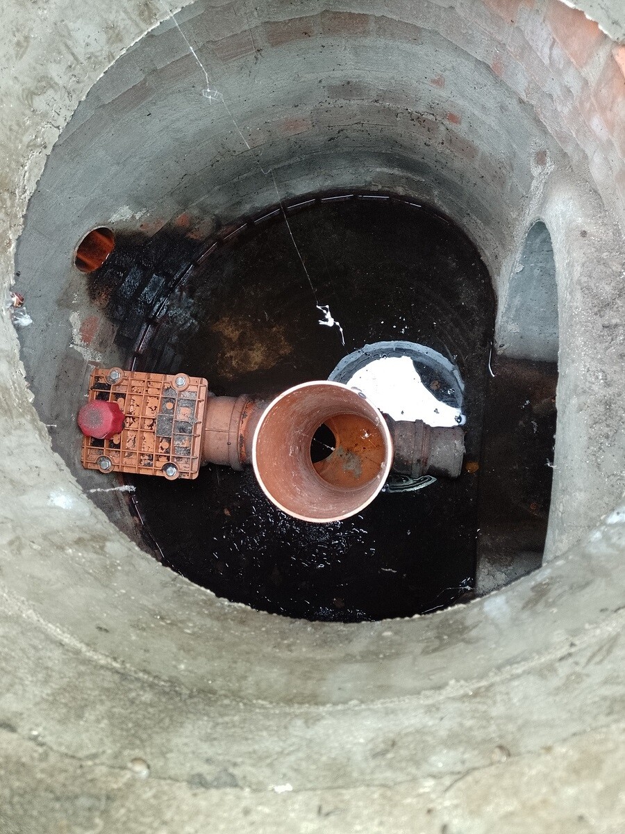 Open concrete shaft with large copper pipe connection and valve actuator in water.