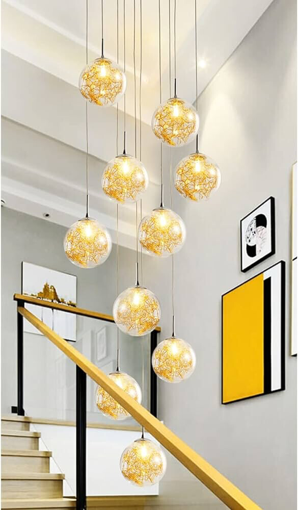 Several yellow glass globe lamps hanging over a wooden staircase with railing and wall art.