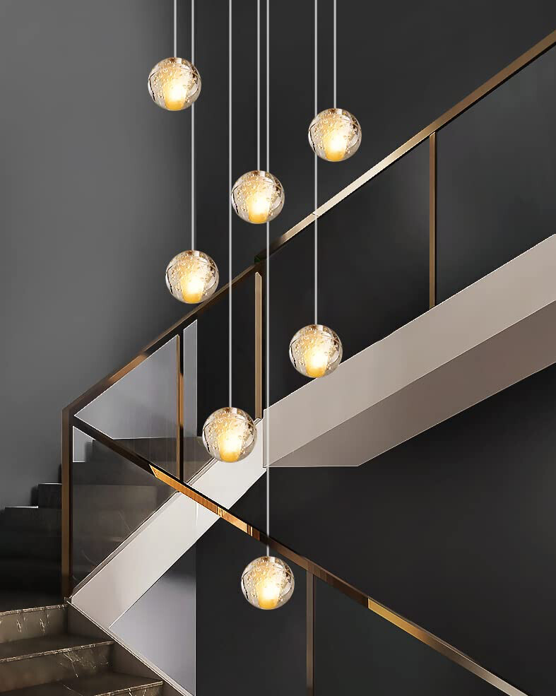 Modern staircase with glass railing and hanging glass globe lamps with gold accents.