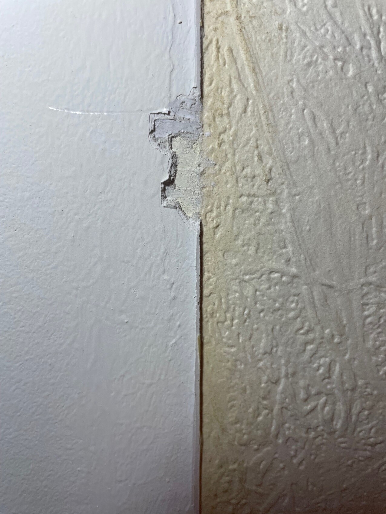 Joint area: white smooth surface meets beige, coarsely textured wall; small chipping.